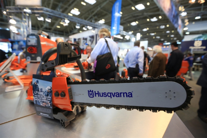 A Husqvarna branded chainsaw sitting on a table, with people in the background.