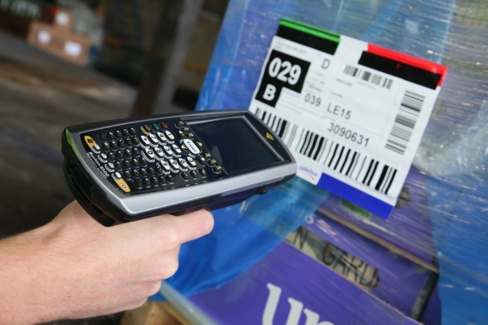 A user with a handheld scanner scanning a barcode on packaging.